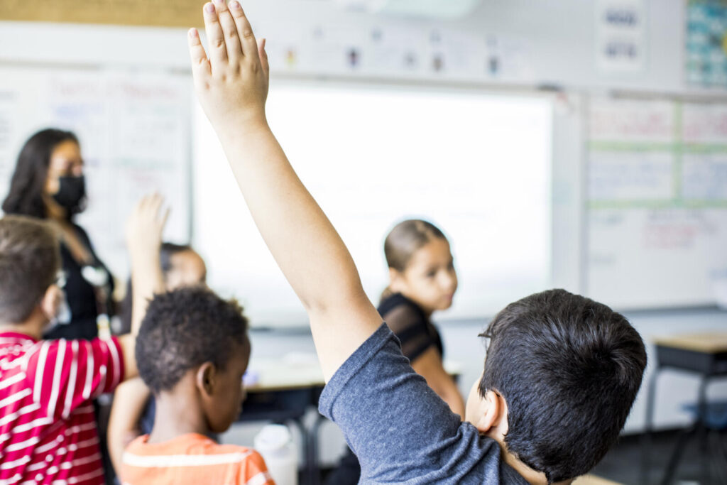 A student in a classroom with their hand raised.