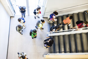 The view from above of students walking through a door and up a flight of stairs.