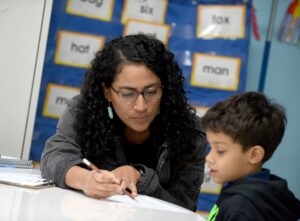 A woman with a pencil in her hand sits at a table with an elementary-aged student.