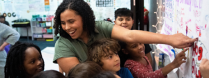 Teacher and students point to a drawing on a white board