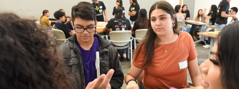 A group of students huddle around a table and have a lively discussion.