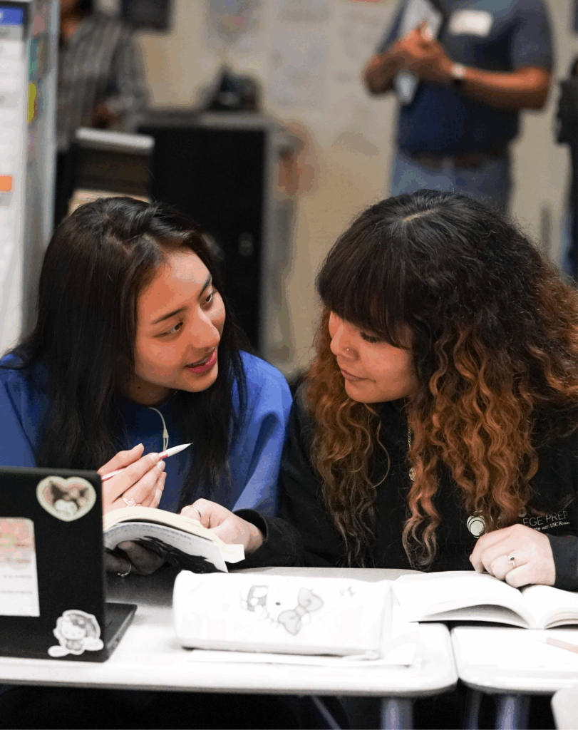 Three students sit side-by-side, reading open books and engaging in discussion.