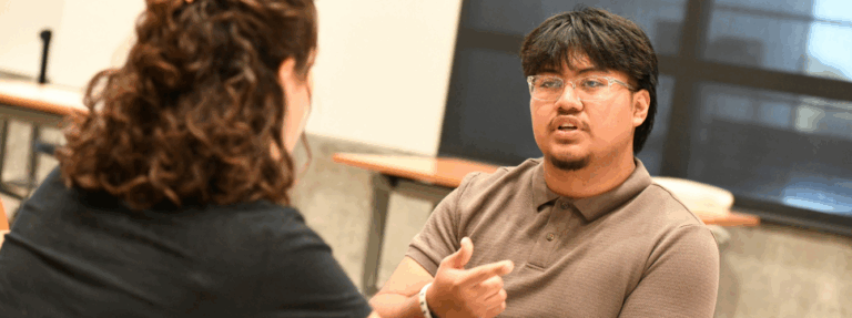 A high school senior speaks with an adult sitting next to him.