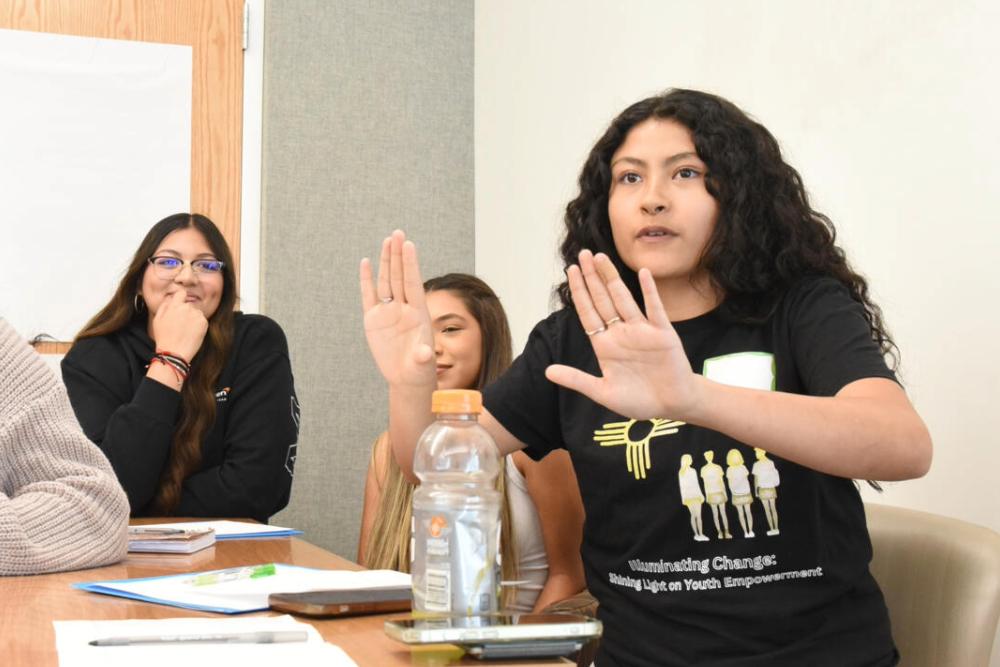 Alt text: A group of students huddle around a table and have a lively discussion.