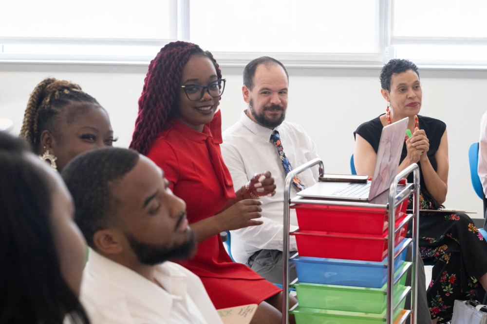 A coach and teachers seated in a classroom, engaged in a discussion.