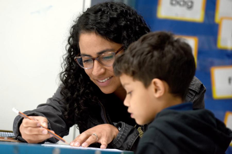 A woman with a pencil in her hand sits at a table with an elementary-aged student.