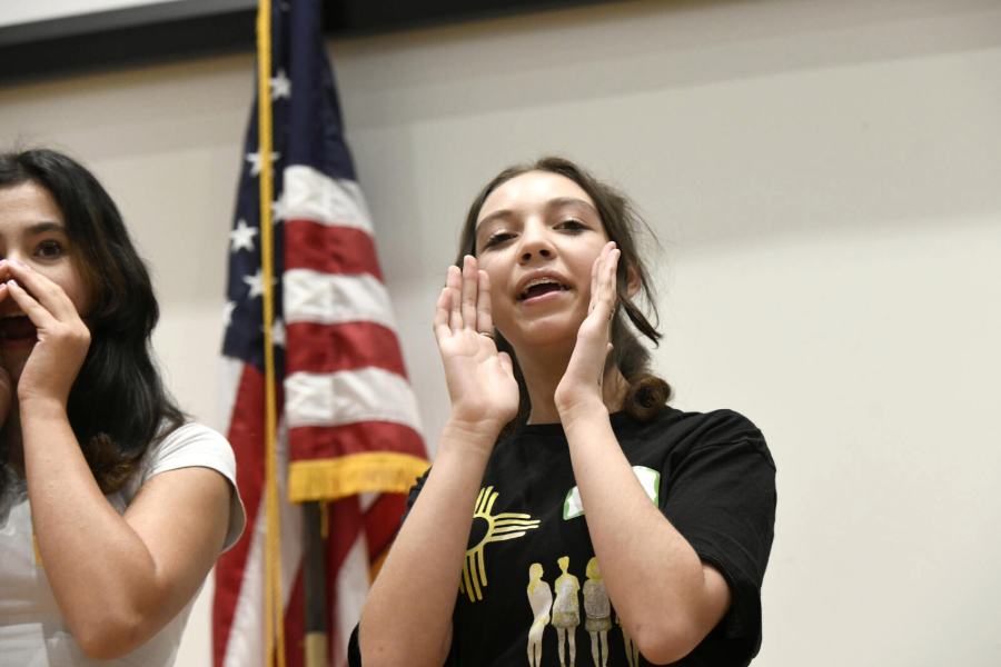 A young person cups her hands around her mouth and calls out to the others in the room.