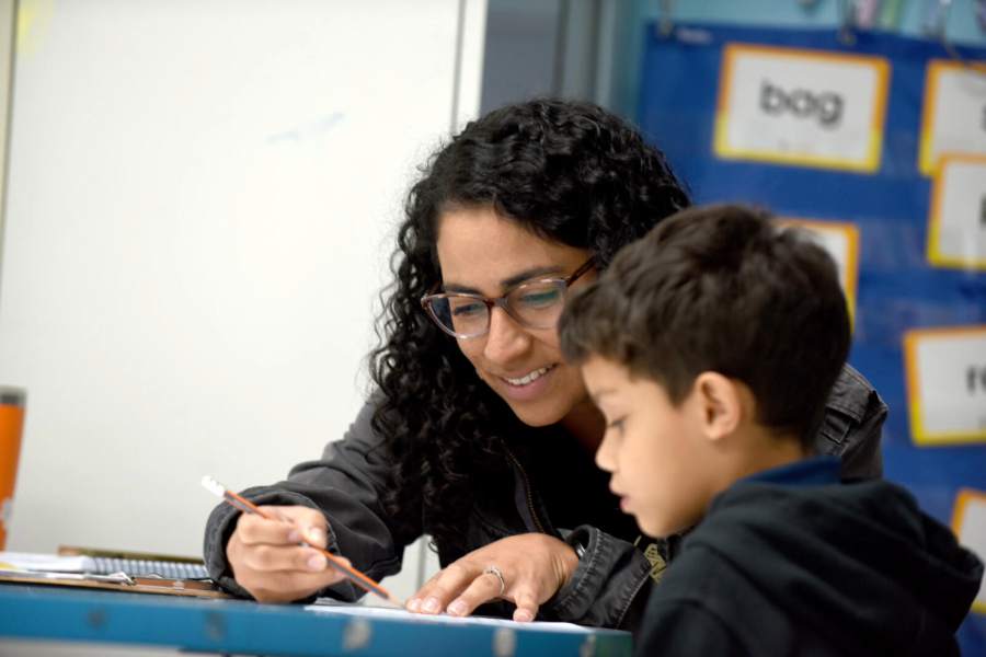 A woman with a pencil in her hand sits at a table with an elementary-aged student.