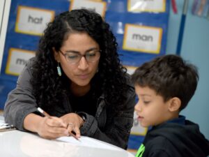 A woman with a pencil in her hand sits at a table with an elementary-aged student.