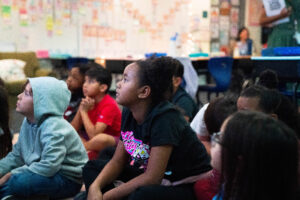 Students sit together on a classroom carpet.