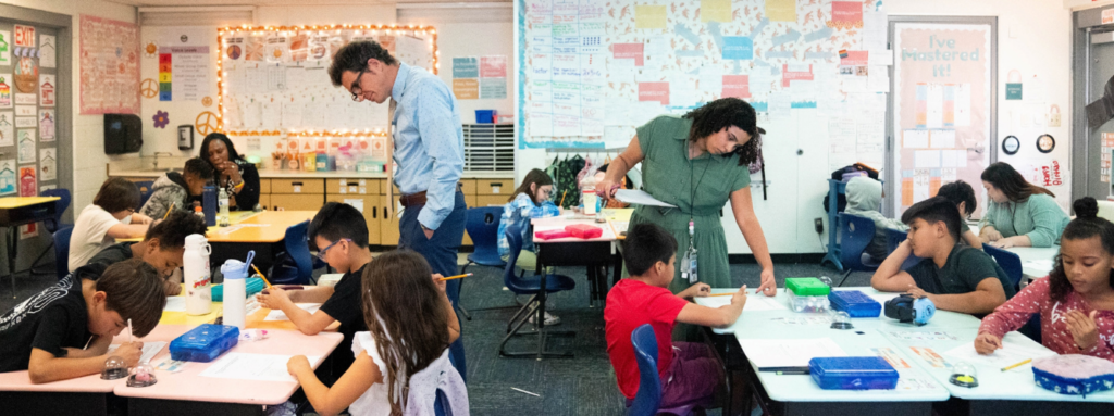 A teacher and principal observe students working at their desks.