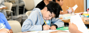 Child writes on a worksheet in a classroom.