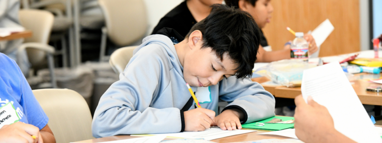 Child writes on a worksheet in a classroom.