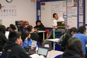 A classroom of students follow along with their teacher.