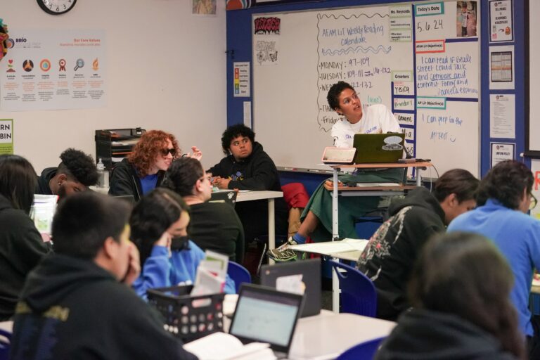A classroom of students follow along with their teacher.