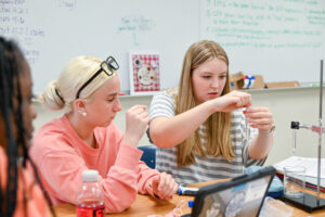 Teenage students look on at a science experiment as one of them holds a test tube